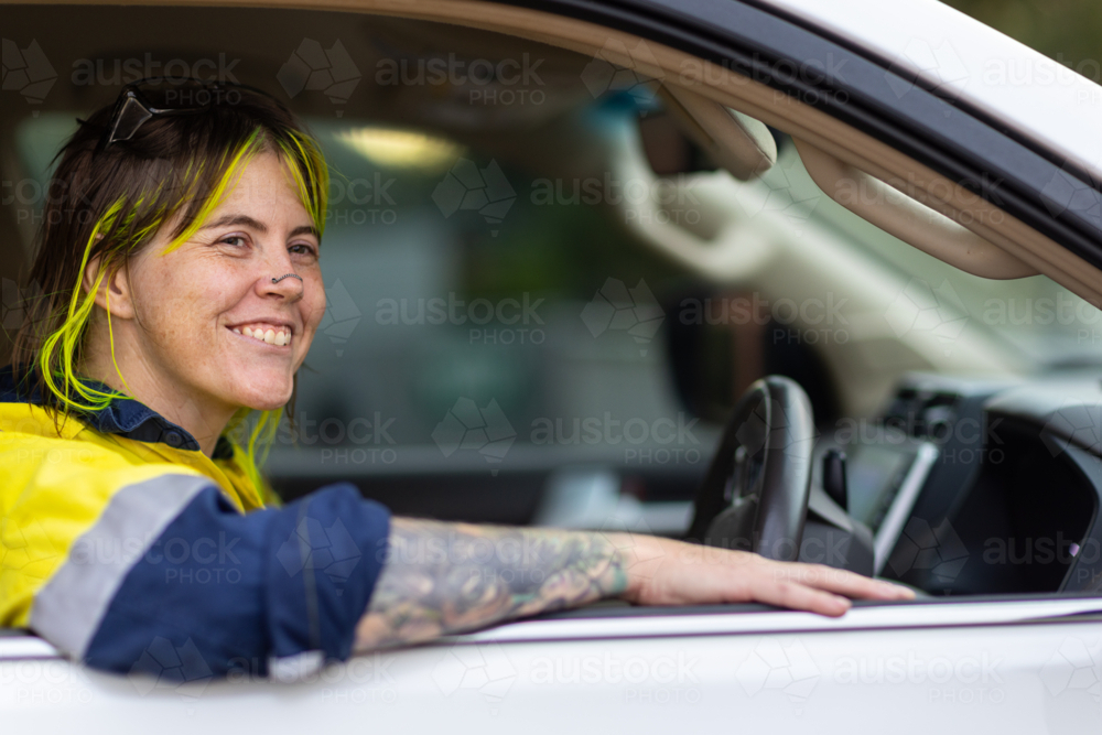 alternative-looking female tradie with bright hair highlights and nose chain in driver's seat of car - Australian Stock Image