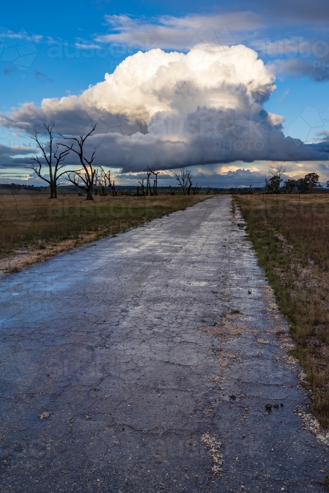 An abandoned road heading into the distance under a large storm cloud - Australian Stock Image