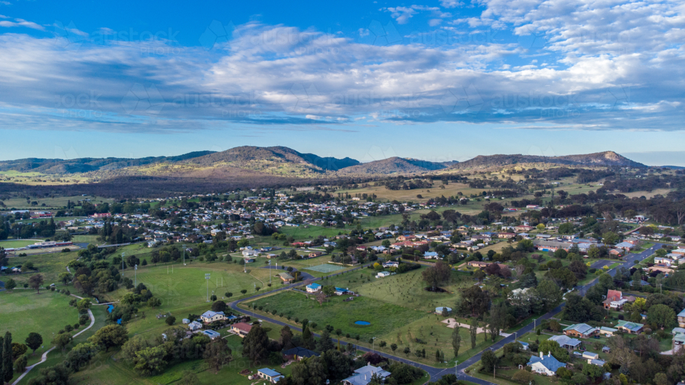 An aerial photo of a country town with green grass underneath a cloudy blue sky - Australian Stock Image