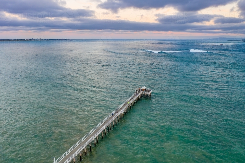 An aerial view of a long narrow jetty jutting out into the ocean on an overcast day - Australian Stock Image