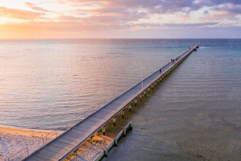 An aerial view of a long narrow jetty jutting out to sea at sunset - Australian Stock Image
