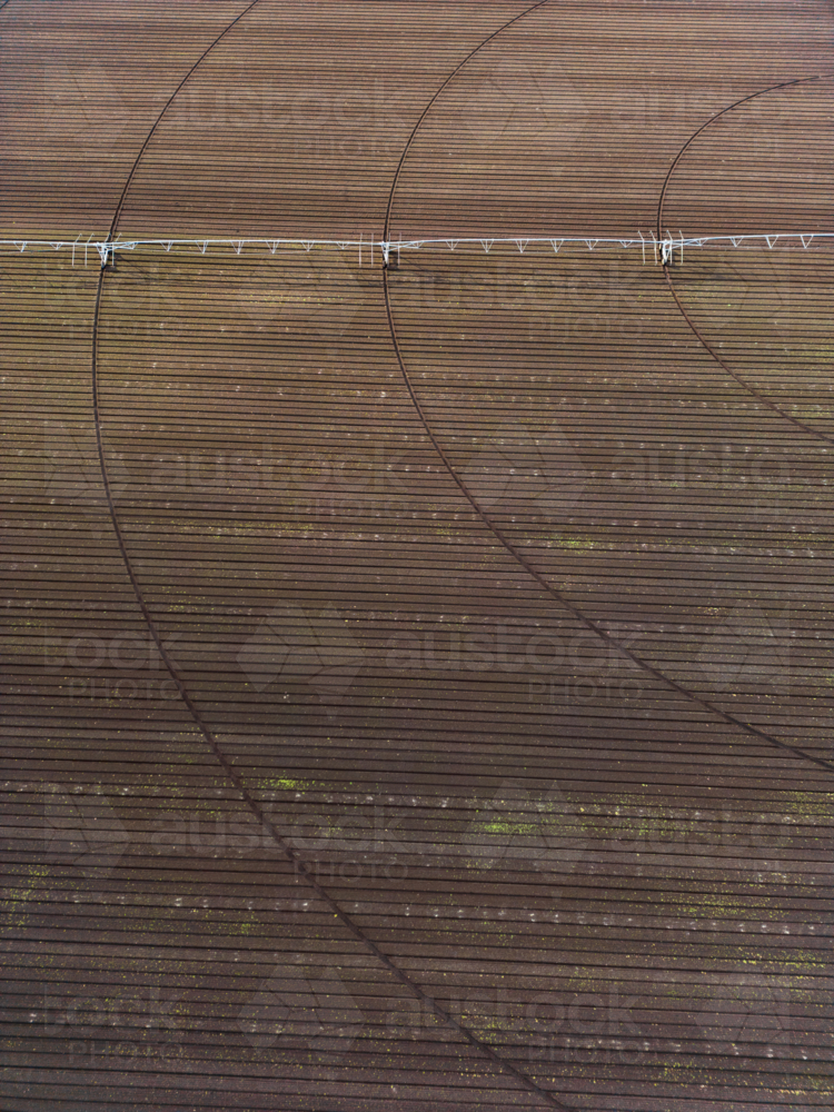 An aerial view of a ploughed deep brown soil field with a centre-pivot irrigator sitting on it - Australian Stock Image