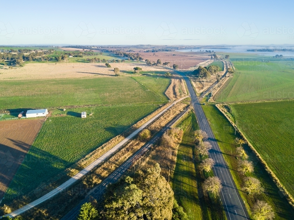 An aerial view of roads and a railway line intersecting through green farmland - Australian Stock Image