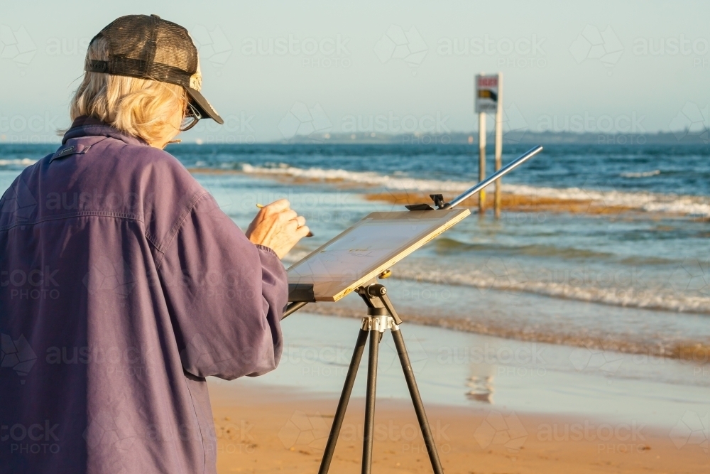 An artist painting on an easel on a beach - Australian Stock Image