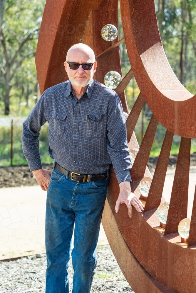 An artist standing proudly in front of a large metal sculpture - Australian Stock Image