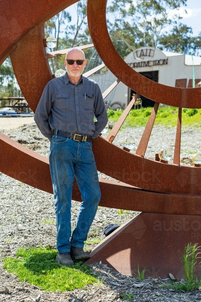 An artist standing proudly in front of a large metal sculpture - Australian Stock Image