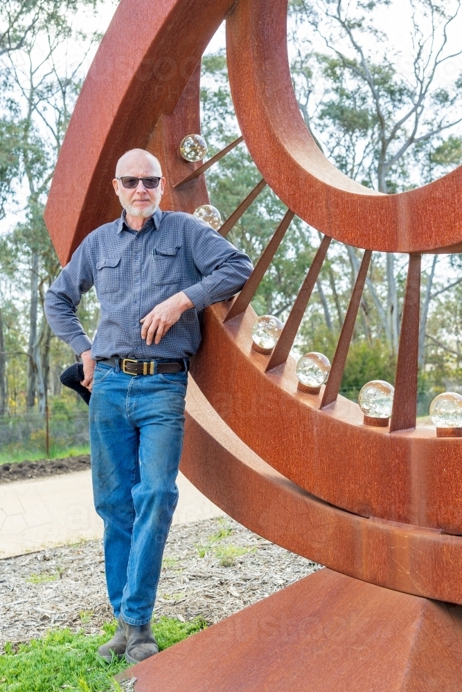 An artist standing proudly in front of a large metal sculpture - Australian Stock Image