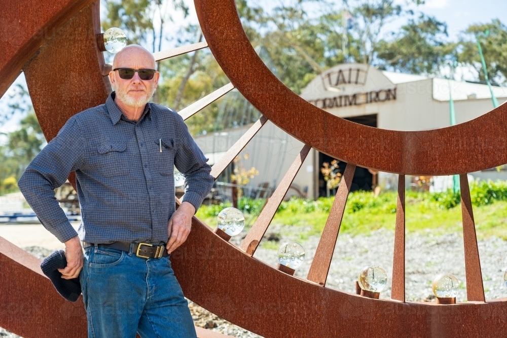 An artist standing proudly in front of a large metal sculpture - Australian Stock Image