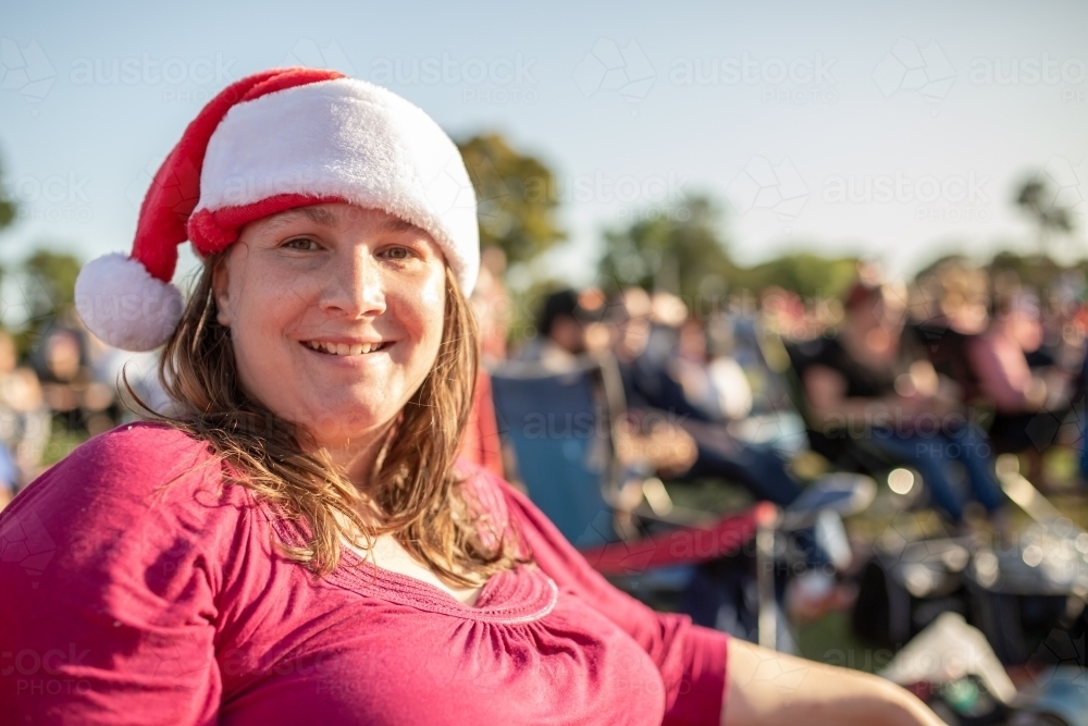 An Australian caucasian woman wearing a Santa hat at outdoor Christmas carols in the summer - Australian Stock Image