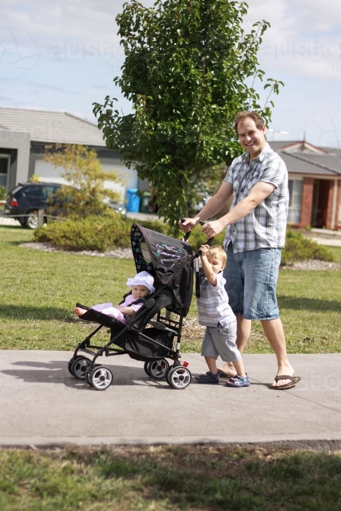 An Australian father pushing a baby in a pram with his toddler son on a warm sunny day - Australian Stock Image