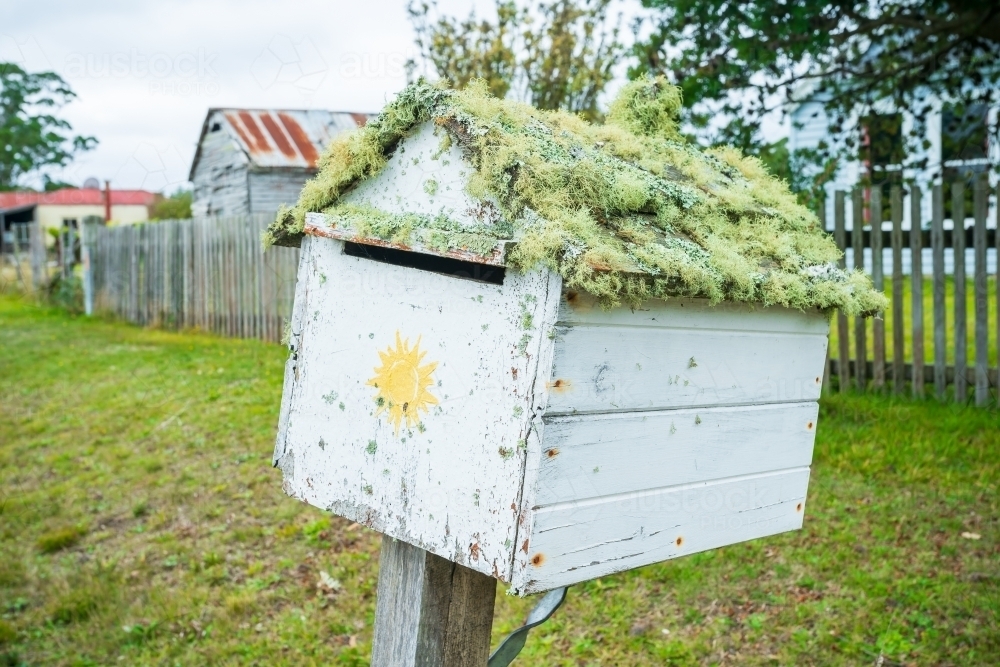 An crooked wooden letterbox with moss growing on it near a front fence. - Australian Stock Image