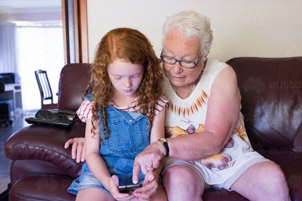 An elderly lady and young child playing on a smartphone - Australian Stock Image