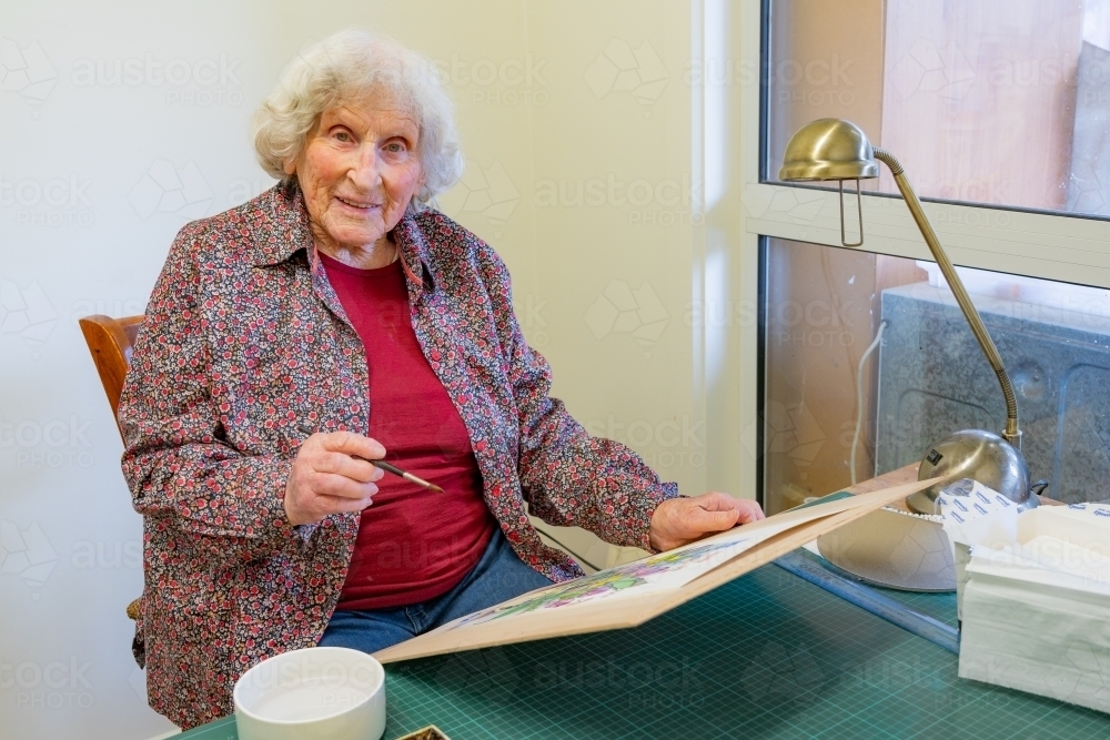 An elderly lady artist sitting at her work with a brush in her hand - Australian Stock Image