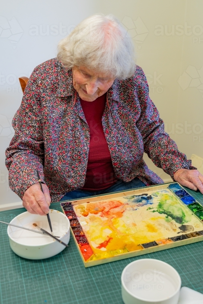Image of An elderly lady artist washing a paint brush in a bowl of
