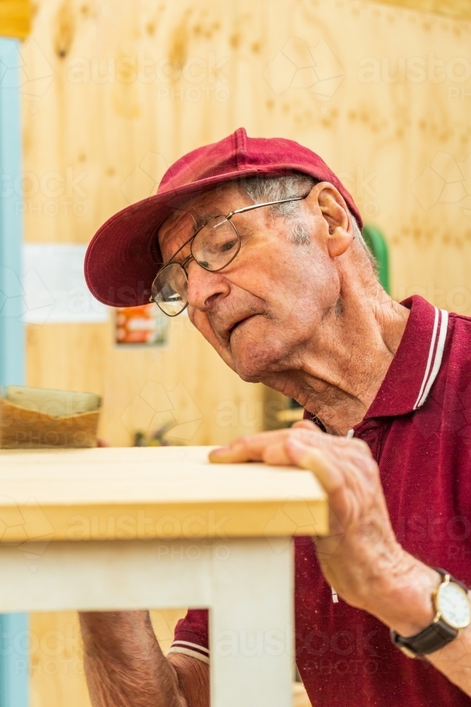 An elderly man sanding a piece of wood at a Men's shed. - Australian Stock Image