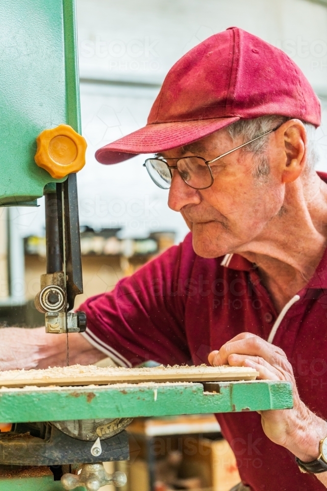 An elderly man sawing a piece of wood at a Men's shed. - Australian Stock Image