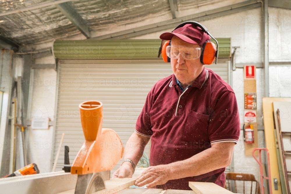 An elderly man sawing a piece of wood at a Men's shed. - Australian Stock Image