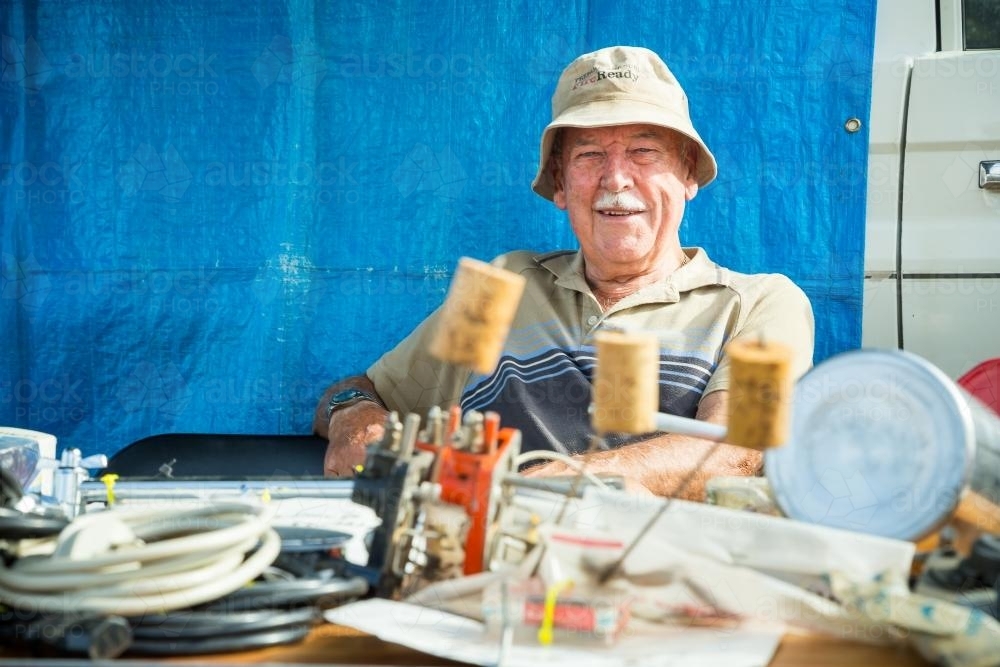 An elderly man sitting behind his stall at a swap meet - Australian Stock Image