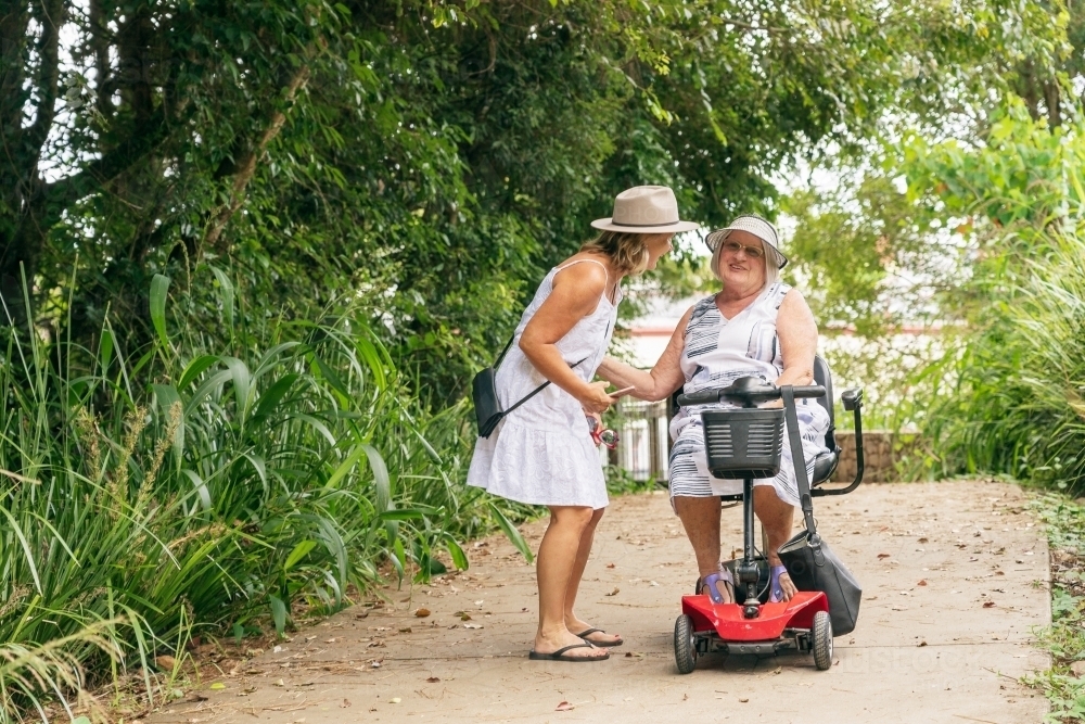 An elderly woman on a disability scooter laughing with her daughter on a path through a park - Australian Stock Image