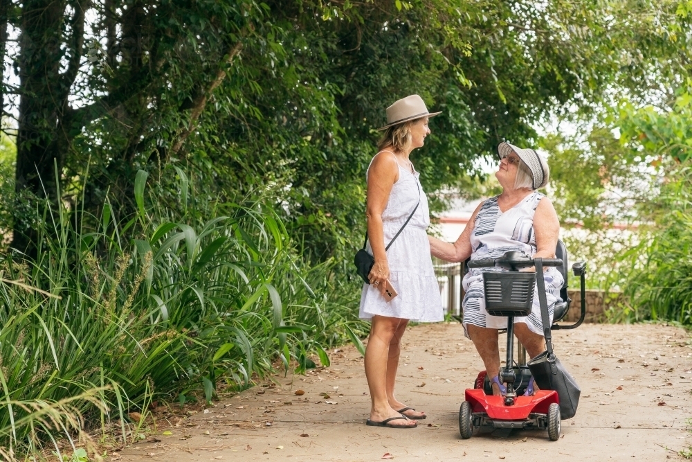 An elderly woman on a disability scooter with her daughter walking down a path in a park - Australian Stock Image