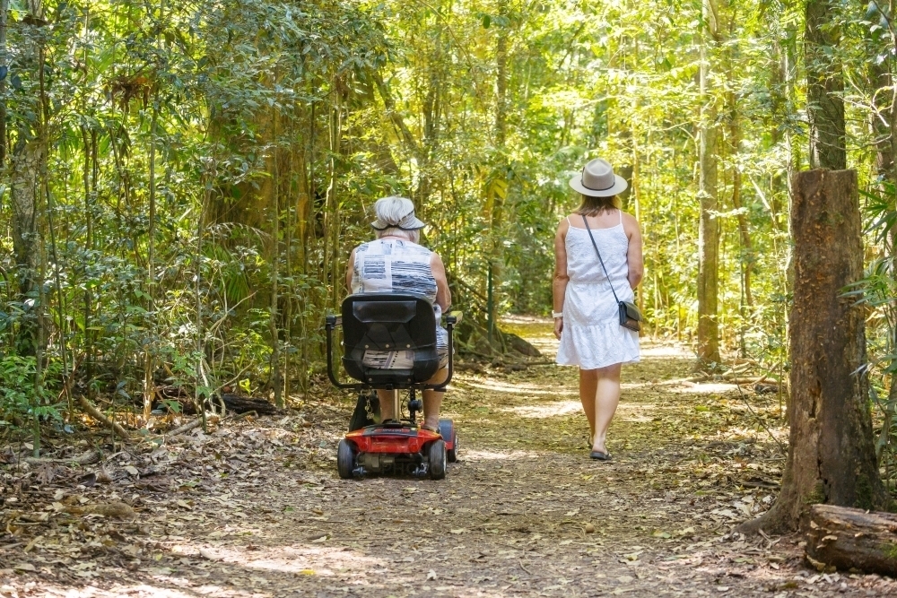 An elderly woman on a disability scooter with her daughter walking through a rainforest - Australian Stock Image