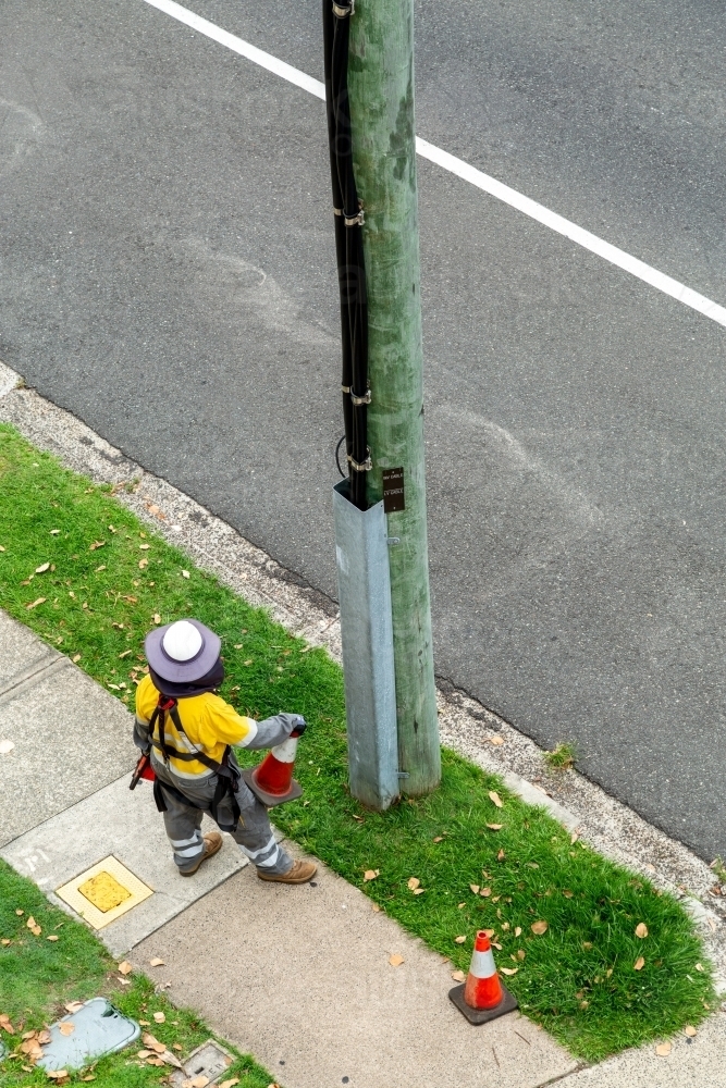 An electric power line worker stands at base of wooden power pole. - Australian Stock Image