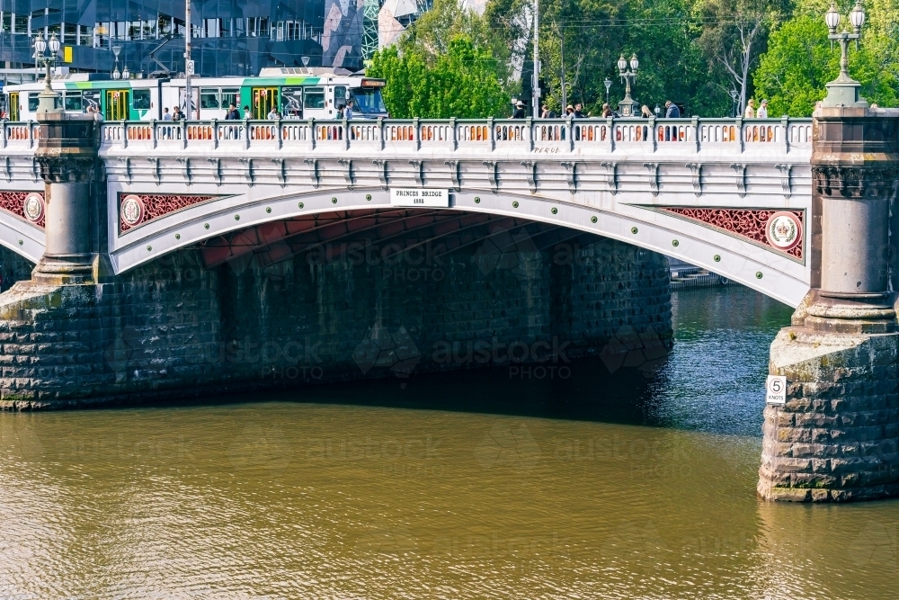 An electric tram crossing an historic arched bridge over a river - Australian Stock Image
