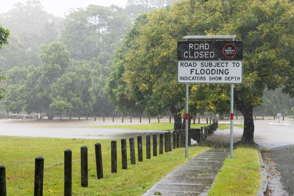 An electronic street sign saying road closed due to flooding with water in background - Australian Stock Image