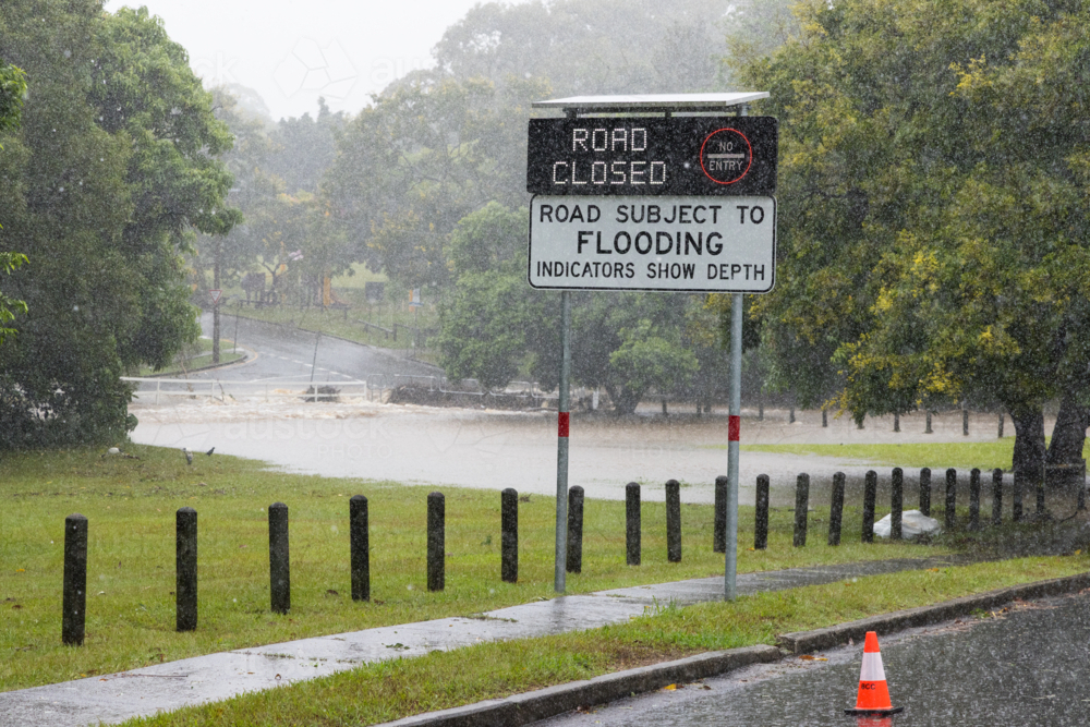 An electronic street sign saying road closed due to flooding with water in background - Australian Stock Image