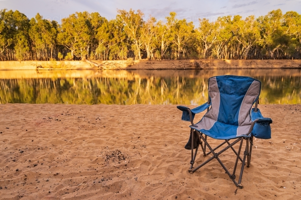 An empty camp chair sitting on a sandy river bank - Australian Stock Image
