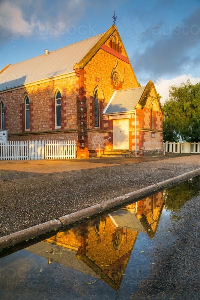 An historic brick church reflected in roadside puddles - Australian Stock Image