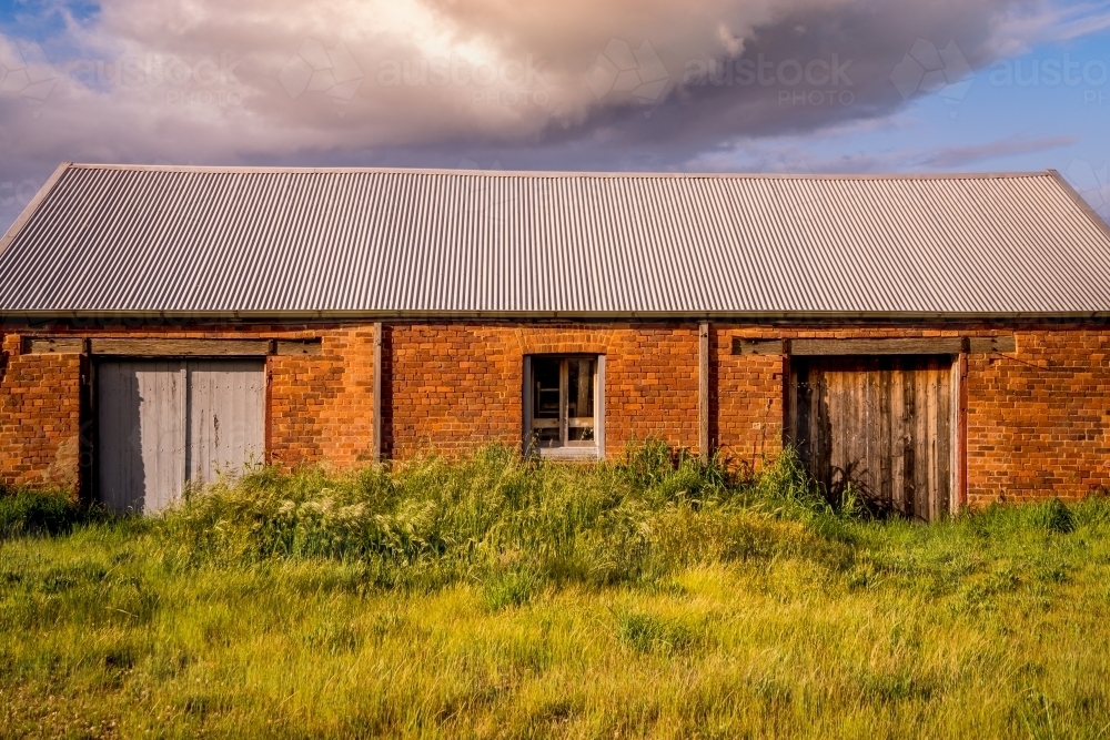 An old brick barn with a colourful cloud overhead - Australian Stock Image