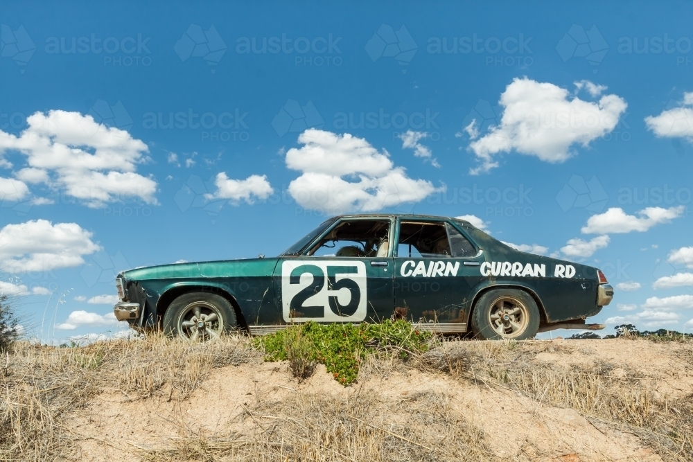 An old car sitting up on a mound of dirt against a blue sky - Australian Stock Image