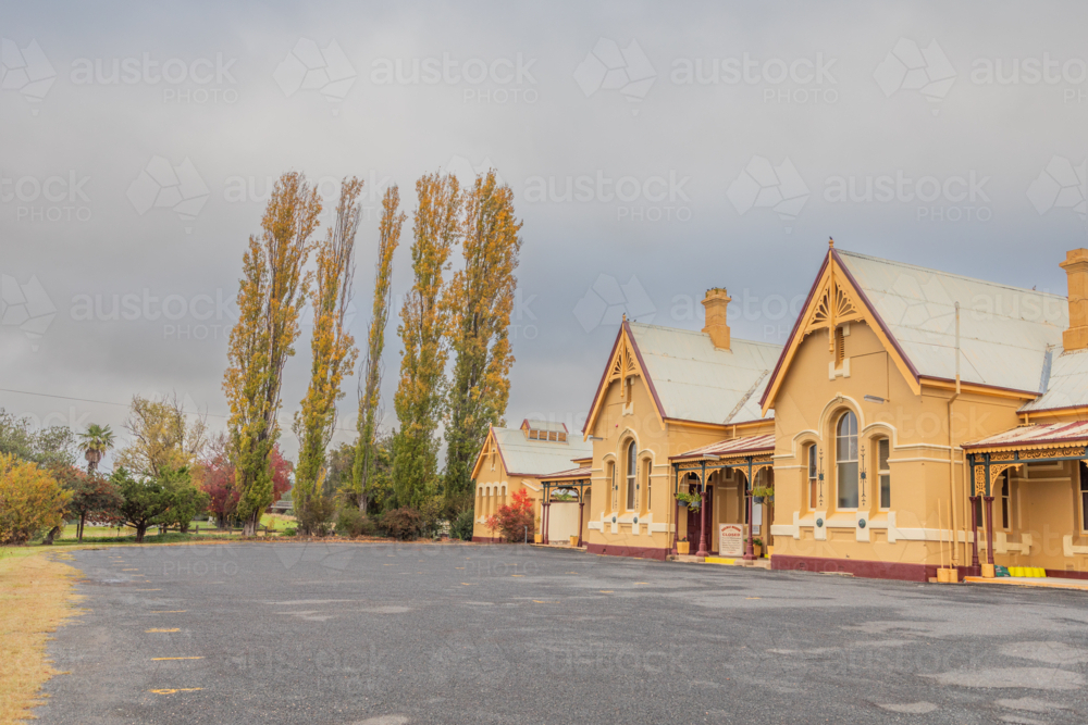 An old country railway building with a tree with autumn foliage - Australian Stock Image