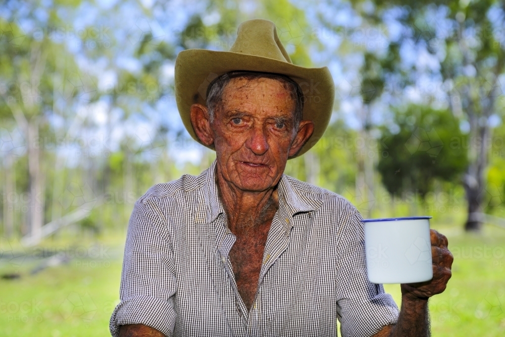 An old drover aged 84 enjoying his morning cup of tea under the shade of trees in the bush. - Australian Stock Image