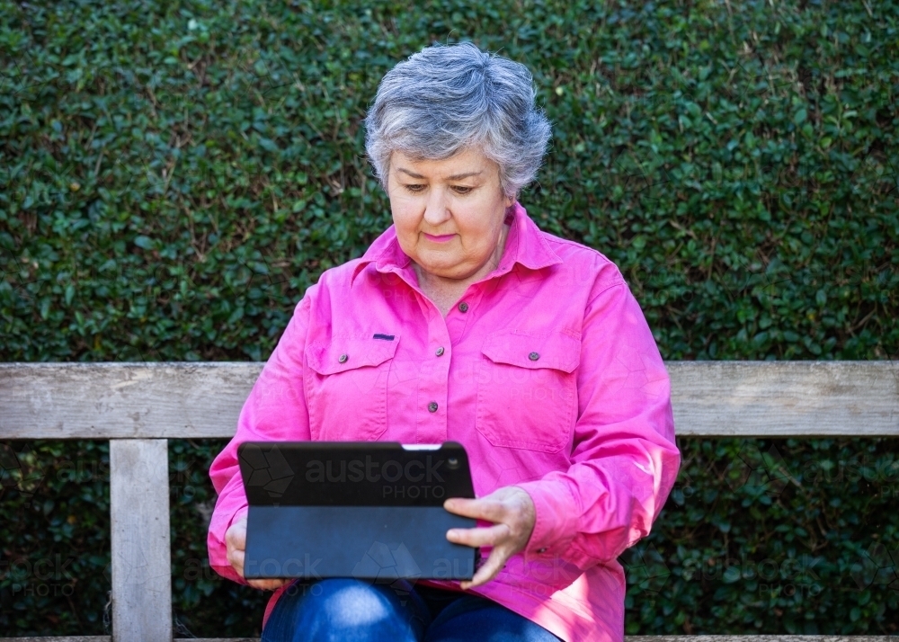 An old lady sitting on the bench using her tablet - Australian Stock Image