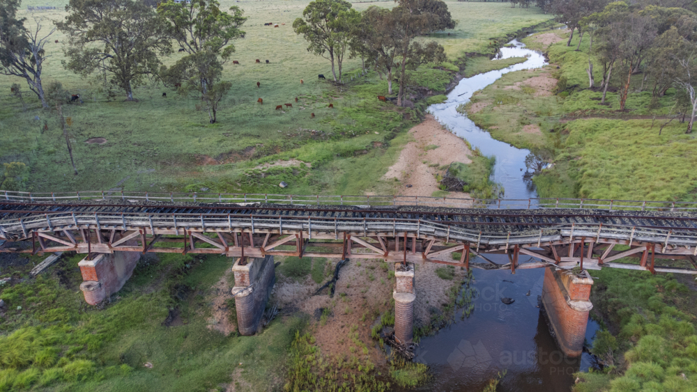 An old railway bridge from above over a meandering creek through a paddock - Australian Stock Image
