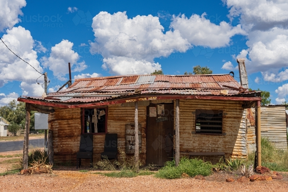 An old, rustic corrugated iron miners cottage under fluffy white clouds in a blue sky - Australian Stock Image