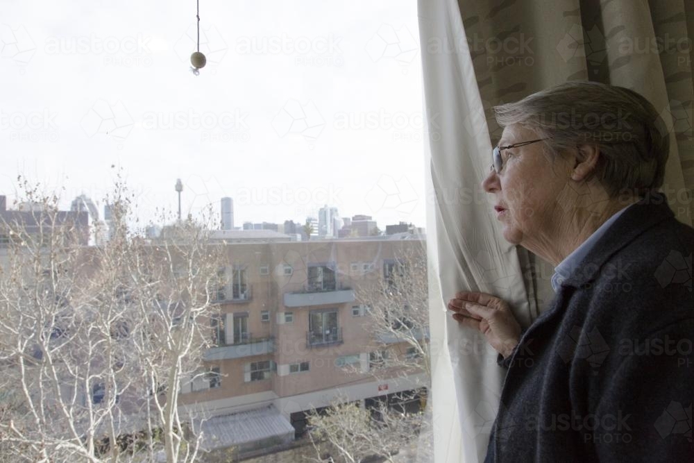 An older woman looks out a window at the sydney city skyline - Australian Stock Image