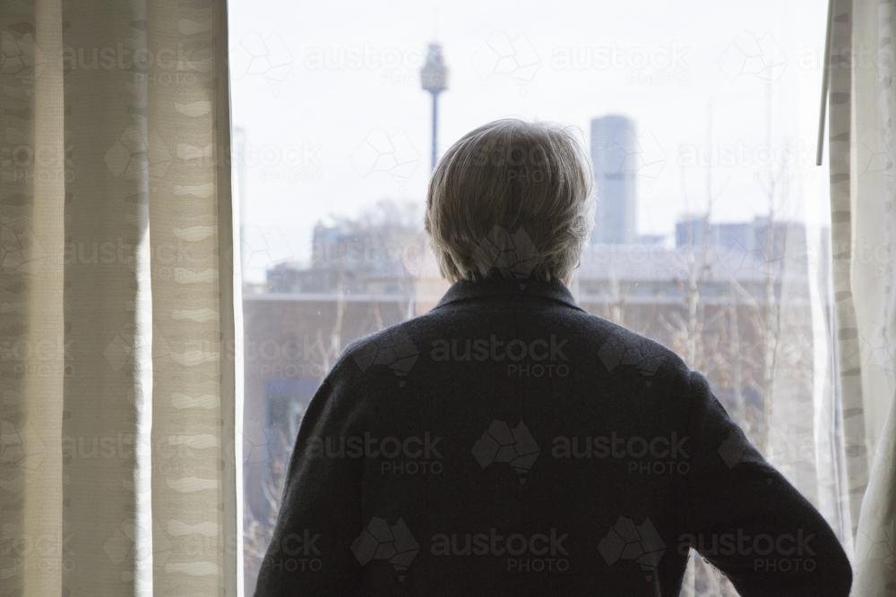 An older woman looks out a window at the sydney city skyline - Australian Stock Image