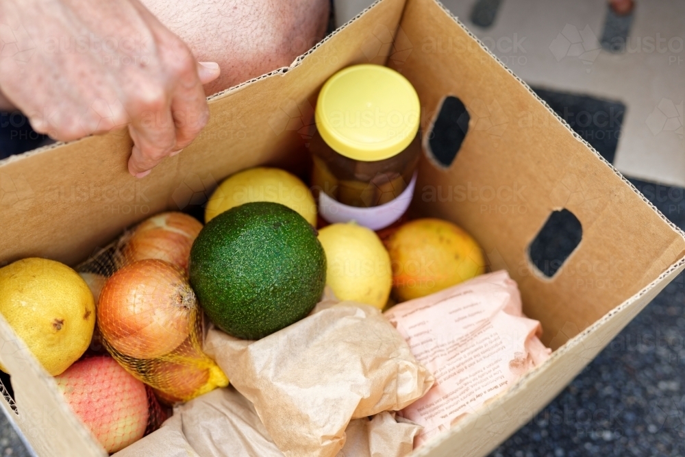 An open box of fresh produce containing honey, avocado, lemons and onions - Australian Stock Image