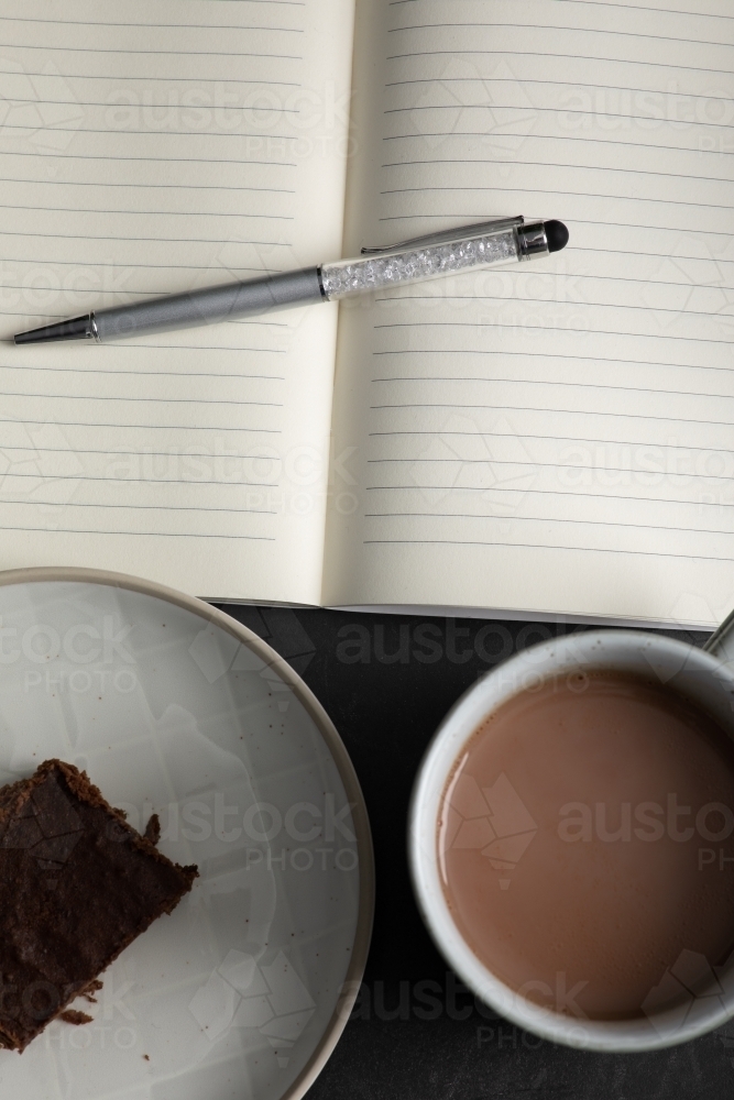 an open notebook with a mug of hot chocolate and piece of chocolate brownie - Australian Stock Image