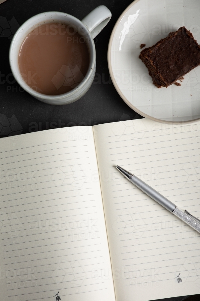 an open notebook with a mug of hot chocolate and piece of chocolate brownie - Australian Stock Image