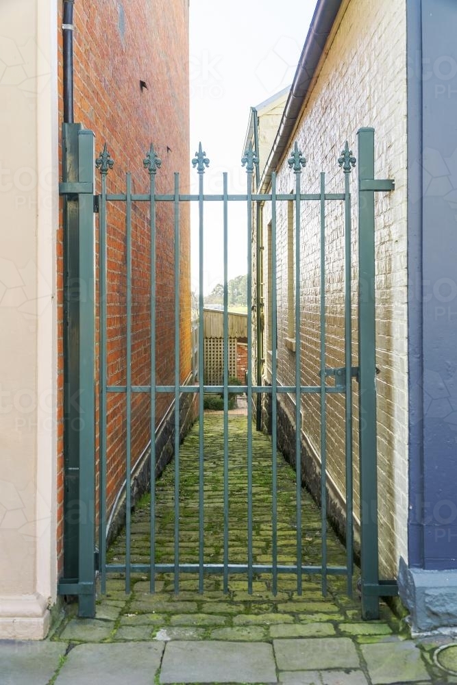 An ornate steel gate blocking a narrow mossy alley - Australian Stock Image