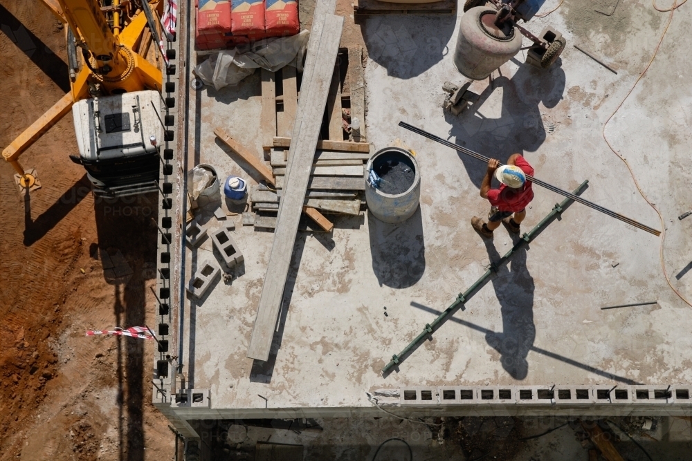 An overhead view of a construction worker carrying a beam on a building site - Australian Stock Image