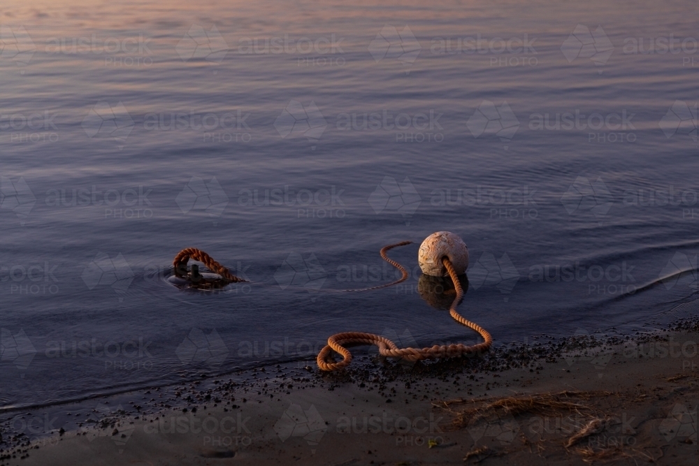 anchor, rope and buoy on edge of lake at dusk - Australian Stock Image
