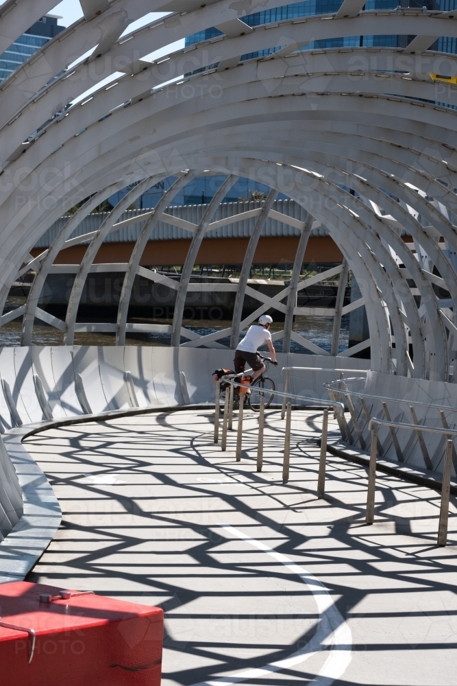 Anonymous cyclist riding through The Net Bridge in Melbourne's Docklands - Australian Stock Image