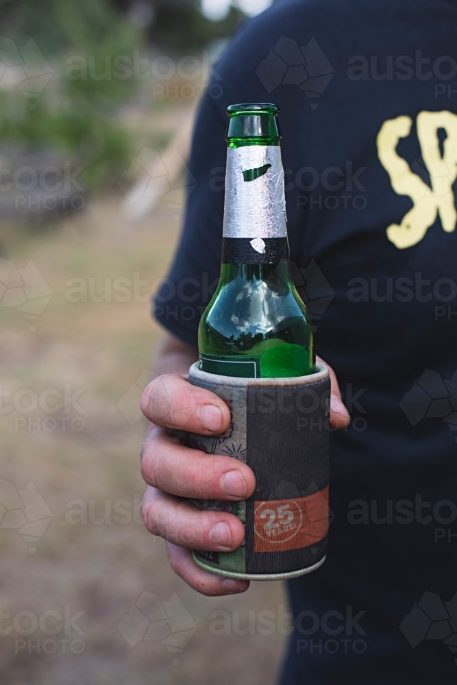 Anonymous man holding beer bottle outdoors in backyard - Australian Stock Image