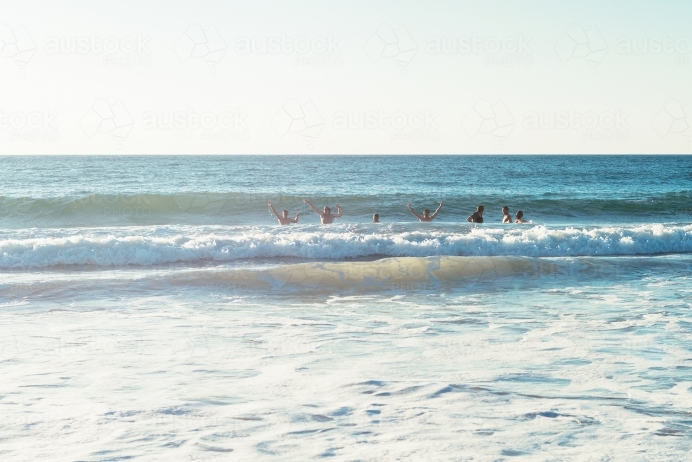 Anonymous young men mucking about in the ocean waves - Australian Stock Image