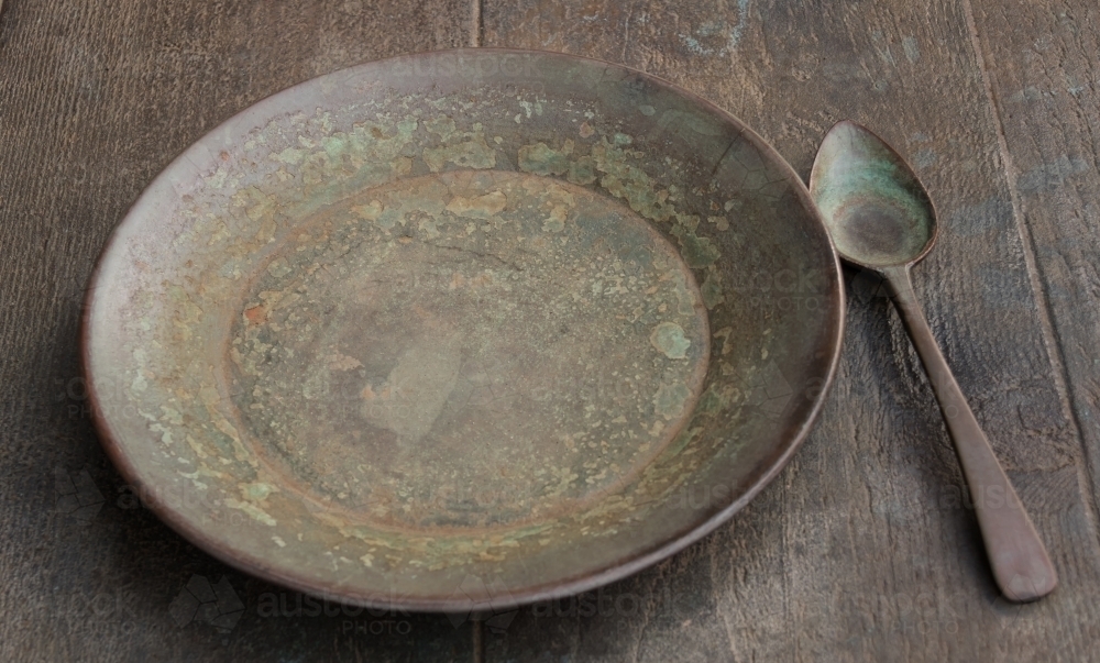 Antique bronze plate & spoon on timber table - Australian Stock Image